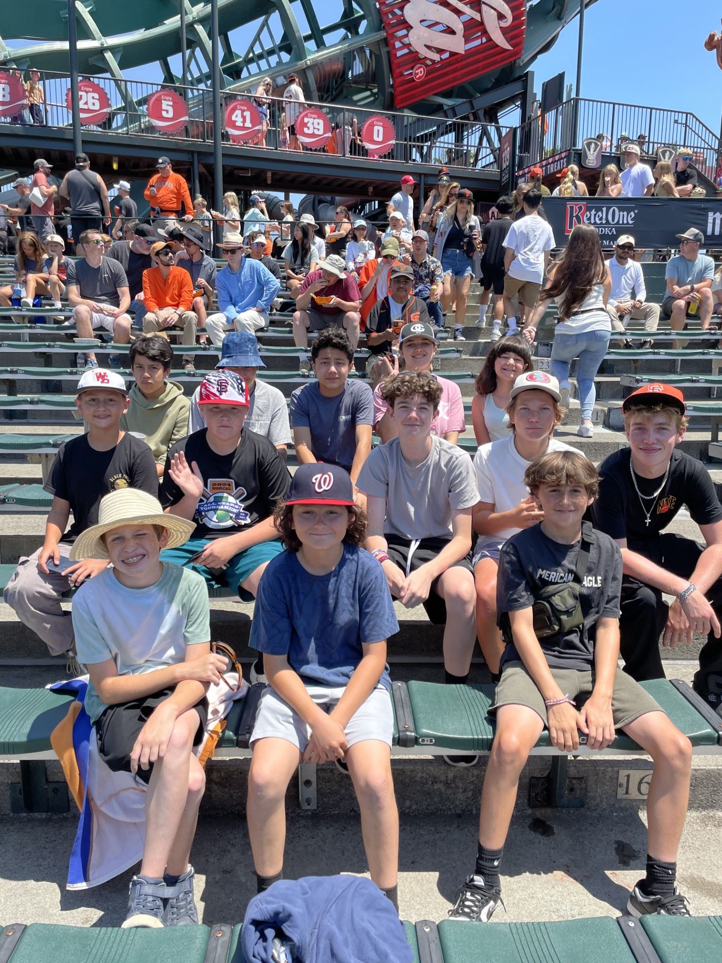 group of kids smiling in the bleachers of a baseball stadium